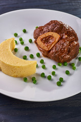 Unusual serving of food in a cafe, restaurant. Potato puree / polenta in the form of an incomplete moon, green peas in the form of stars in the sky. A large piece of appetizing meat on the bone.