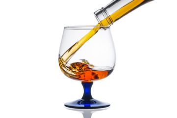 Brandy pouring from bottle into glass on white background
