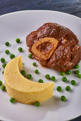 Unusual serving of food in a cafe, restaurant. Potato puree / polenta in the form of an incomplete moon, green peas in the form of stars in the sky. A large piece of appetizing meat on the bone.