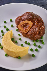 Unusual serving of food in a cafe, restaurant. Potato puree / polenta in the form of an incomplete moon, green peas in the form of stars in the sky. A large piece of appetizing meat on the bone.
