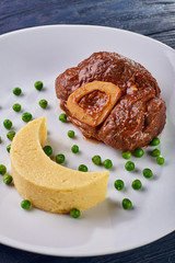 Unusual serving of food in a cafe, restaurant. Potato puree / polenta in the form of an incomplete moon, green peas in the form of stars in the sky. A large piece of appetizing meat on the bone.