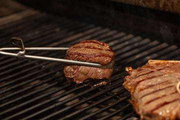 Tongs Holding Grilled Pork Ribs. Hot Flaming BBQ Grill on the Background