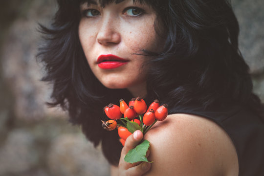 Sexy beautiful pretty brunette with red lipstick with red rose hips in hand