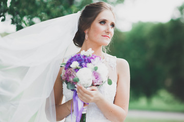 Beautiful bride in elegant white dress holding bouquet posing in park