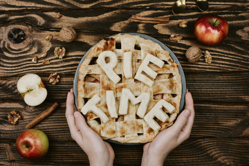 Flatlay of woman's hands holding autumn apple pie with Pie Time letters on top of it on wooden...