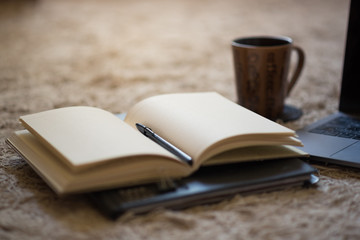 An open journal with pen and warm light illuminating blank pages, coffee mug and laptop in...