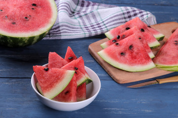 composition with slices of fresh ripe watermelon in a white bowl on a blue wooden table