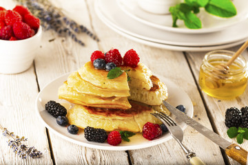 Pancakes with forest fruits berries on white table.