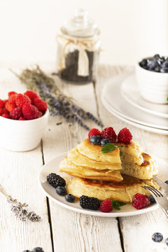 Pancakes with forest fruits berries on white table.