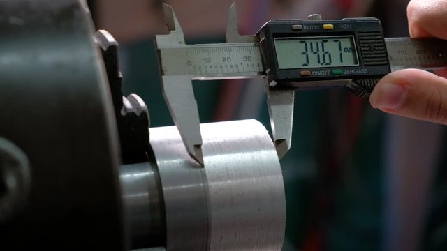 Worker measuring an aluminum metal piece on lathe with calliper