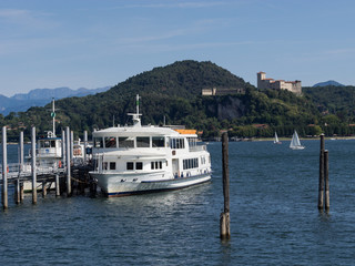 Fototapeta na wymiar Schiffsanleger mit weißem Dampfer und Burg im Hintergrund, Arona, Lago Maggiore, Italien