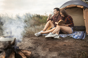 beautiful guy and girl dressed in red checkered shirts sitting on the ground near a tent and a fire