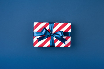 Gift box wrapped in red striped paper and tied with blue bow on dark blue background. Holiday...