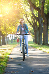 Young woman ride bike in autumn park. Enjoying while cycling in nature during autumn day.