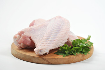 Two wings of turkey on a round wooden board. On the board next to the turkey lies the green of parsley. White background. Close-up.