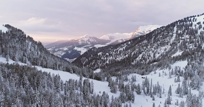 Side aerial to snowy valley with woods forest at Sella pass.Sunset or sunrise,cloudy sky.Winter Dolomites Italian Alps mountains outdoor nature establisher.4k drone flight