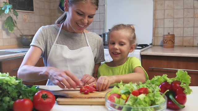 Happy woman with her daughter cooking dinner in the kitchen together.