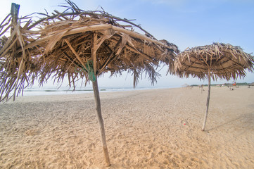Fototapeta na wymiar Thatch umbrellas of straw for shade on paradise beach in pondicherry chennai with brown sand, blue skies and the orange from sunrise making this the perfect vacation shot
