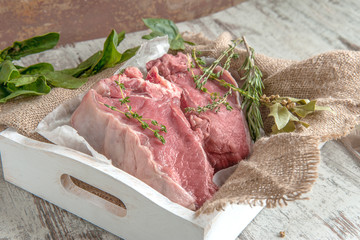 Cuts of beef for grilling on a wooden cutting Board with spinach, rosemary and Provencal herbs for the marinade in a rustic style