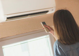 Woman holding remote control aimed at the air conditioner.