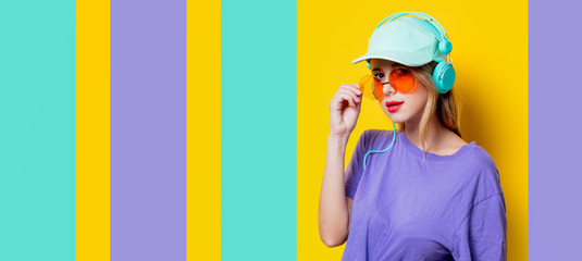 Young style girl with orange glasses and headphones on colored background. Clothes in 1980s style