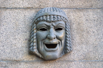 Metal theatrical mask symbolizes humor on the granite fence. Saint-Petersburg.