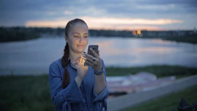 Portrait of young beautiful caucasian woman using smart phone hand hold outdoor in the city night, smiling, face illuminated screenlight - social network, technology, comunication concept