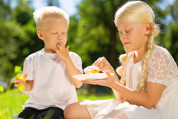 Cakes. Happy excited brother and sister eating a cake while being in the park