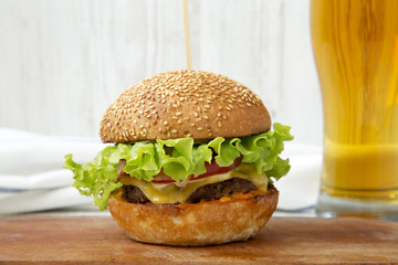 Cheeseburger and glass of beer on white wooden background, side view. Close-up.