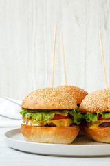 Cheeseburgers on grey plate on white wooden background, side view. Close-up.