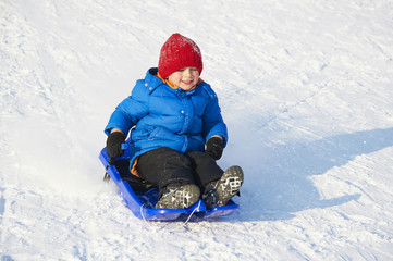 Child boy riding a bobsled. Having fun on the snow. Children winter activities.