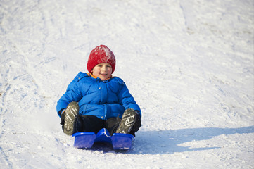 Fototapeta na wymiar Child boy riding a bobsled. Having fun on the snow. Children winter activities.