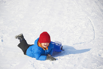 Fototapeta na wymiar Child boy crashed on a bobsled. Having fun on the snow. Children winter activities.