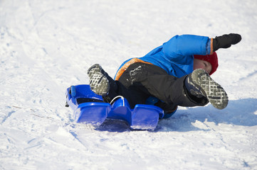 Child boy crashed on a bobsled. Having fun on the snow. Children winter activities.