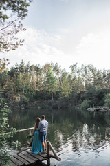 Fototapeta na wymiar A pair of lovers on a bridge near a lake in a pine forest looking at the water surface
