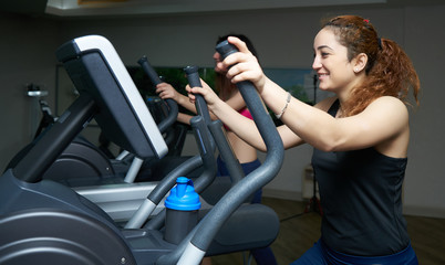 Athletic girl doing an ellipsoid in gym side view. Woman trains on an ellipsoid. Sport and healthy...