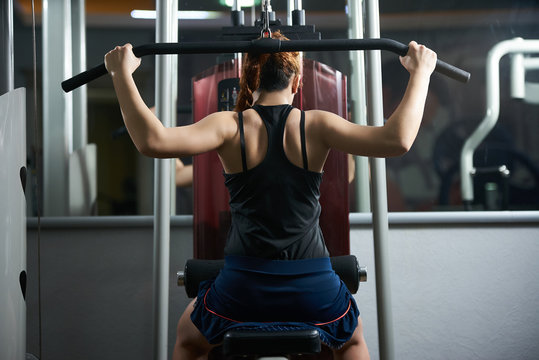 Young Fit Woman Flexing Muscles On Gym Machine In Front Of A Mirror. Sport, Fitness, Strength Training