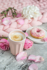 Fototapeta na wymiar Cup with cappuccino, doughnut, pink pastel giant blanket, flowers, bedroom, morning concept