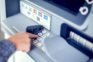 Finance, money, bank and people concept - close up of hand entering pin code at atm machine