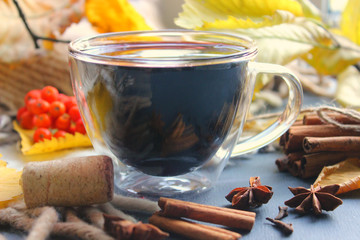 A Cup of mulled wine surrounded by yellow autumn leaves and spices, cinnamon sticks, anise, cloves. Warm warming drink, comfort, relaxation, relaxing drink.