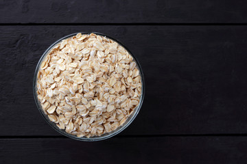 Oatmeal on black background. Flakes of oatmeal on wooden boards. Healthy food. Preparation of breakfast from natural product. Copy space