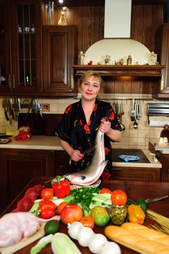 middle-aged woman in the kitchen with a big fish, going to cook
