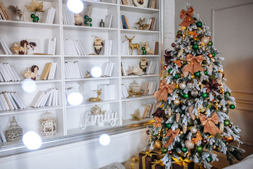 The bedroom decorated for Christmas. Cozy home interior. New year decoration. White room with large bookshelves.. Christmas tree with shyning garland