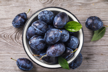 Metal bowl full of ripe prune fruit on a wooden table, top view