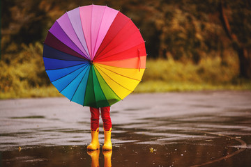 happy child girl with an umbrella and rubber boots in puddle  on autumn walk