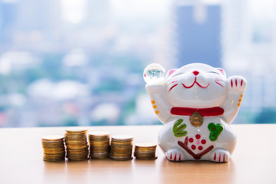 lucky cat holding glass ball and row of gold coin money on blur background