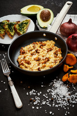delicious scrambled eggs with chanterelles straight from the forest in a pan and bread with avocado on a wooden kitchen table