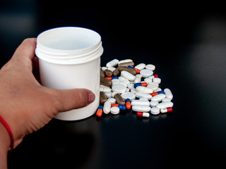 A person holding pills of different sizes, shapes and colors with his hand. Health concept