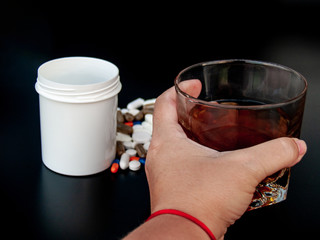 A person with a glass of whiskey in his hand and pills of different sizes, shapes and colors. Concept of drugs and alcohol