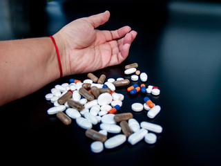 A person holding pills of different sizes, shapes and colors with his hand. Health concept